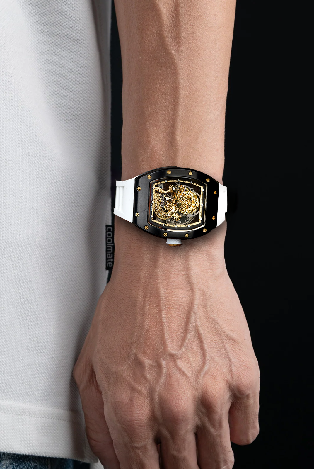 Close-up of a wrist wearing a gold and black watch with a white shirt and blue jeans.